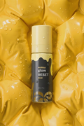 The daezls Midday Glow Reset Mist bottle standing upright on a glossy yellow quilted surface covered in water droplets — highlighting the product's fresh, hydrating identity in a bold, editorial hero shot.