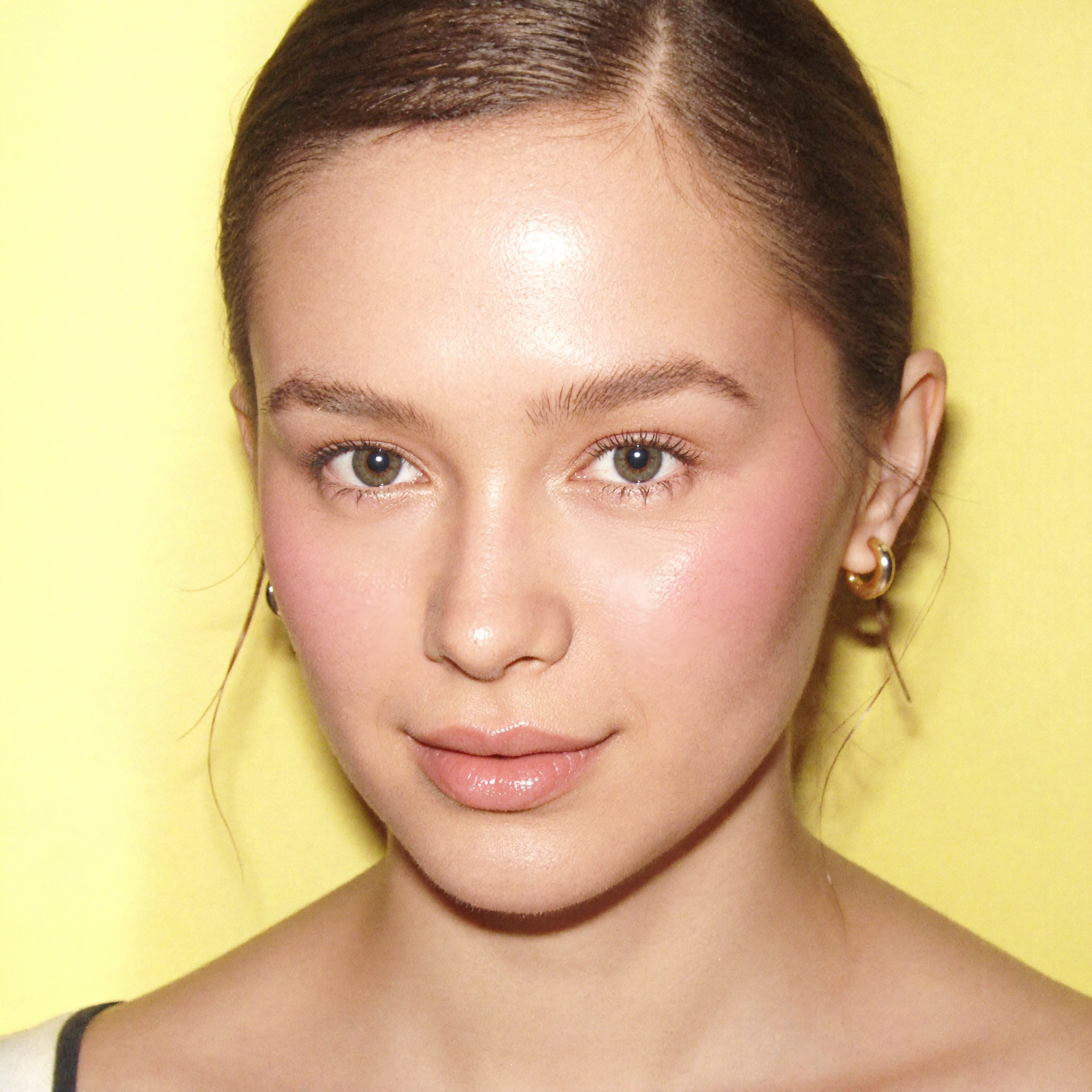 Close-up portrait of a woman with dewy, glowing skin against a bright yellow background — hair pulled back, natural flush, visibly refreshed and hydrated. Captured as an after shot for daezls Midday Glow Reset Mist.
